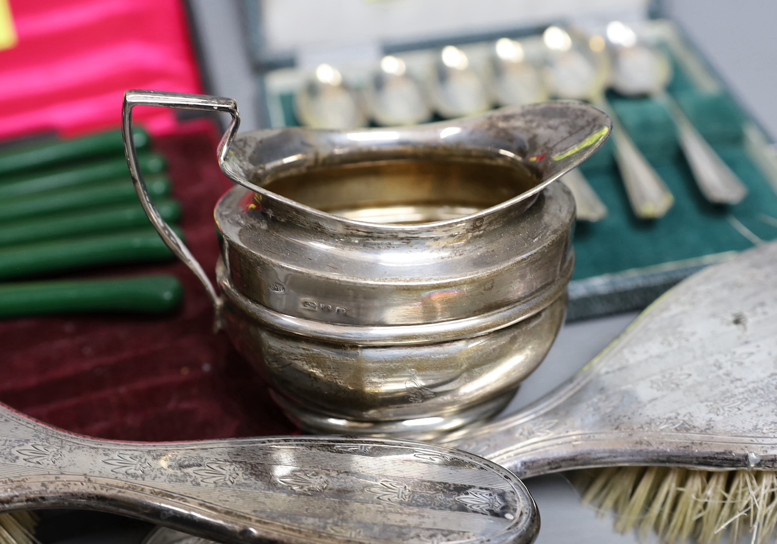 A small group of silver items including a tortoiseshell mounted hand mirror, London, 1917, two silver mounted clothes brushes, a cased set of six teaspoons, a mug and sugar bowl, together with a pair of plated candle snu
